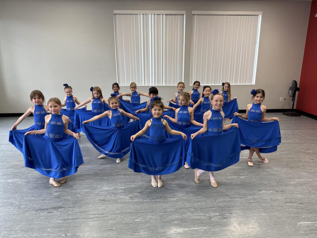 Group of young dancers in matching blue costumes posing together during costume week
