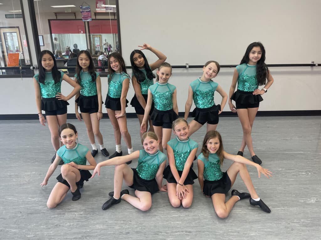 Pre-teen jazz dancers posing in teal sequin costumes during costume week